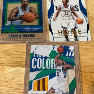 May include: Three trading cards featuring Andrew Wiggins, a basketball player for the Minnesota Timberwolves. The cards are from the 2014-15 season and feature different designs. The first card is a green and blue card with the text "Rookies" and "Prestige". The second card is a white card with the text "Home" and "Timberwolves". The third card is a green, blue, and yellow card with the text "Color" and "Prestige".