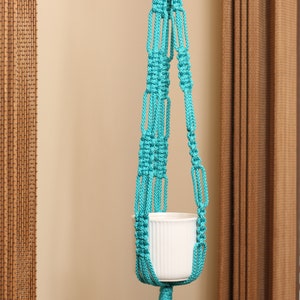 May include: A turquoise macrame plant hanger with a white ceramic pot.