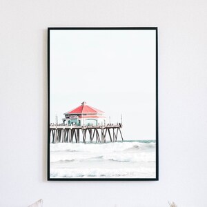 Peut inclure: Une photographie en noir et blanc d'une jetée avec un bâtiment au toit rouge. La jetée est au-dessus de l'océan et des vagues s'écrasent contre elle.