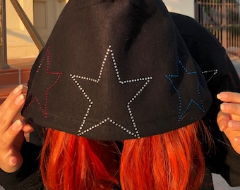 May include: Black hooded sweatshirt with a large star design on the front. The star is outlined with rhinestones and has a red, blue, and white color scheme.