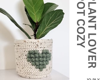 Op de afbeelding: Een gehaakte plantenpot-cozy met een groen hartontwerp. De cozy is gemaakt met een 10-draads garen en is beschikbaar als PDF-patroon. PLANT LOVER POT COZY 10 PLY PDF PATTERN