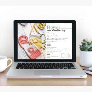 Pode incluir: Um laptop exibe um padr&atilde;o de croch&ecirc; para uma "Flower mini shoulder bag". O padr&atilde;o inclui instru&ccedil;&otilde;es, medidas e uma lista de materiais. A tela mostra imagens das bolsas acabadas em rosa, amarelo e bege.