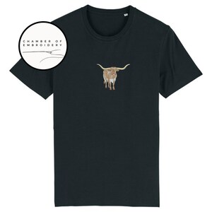 May include: A black t-shirt with a brown and white embroidered longhorn steer on the front. The shirt has a crew neck and short sleeves. The text "Chamber of Embroidery" is in a circle above the steer.
