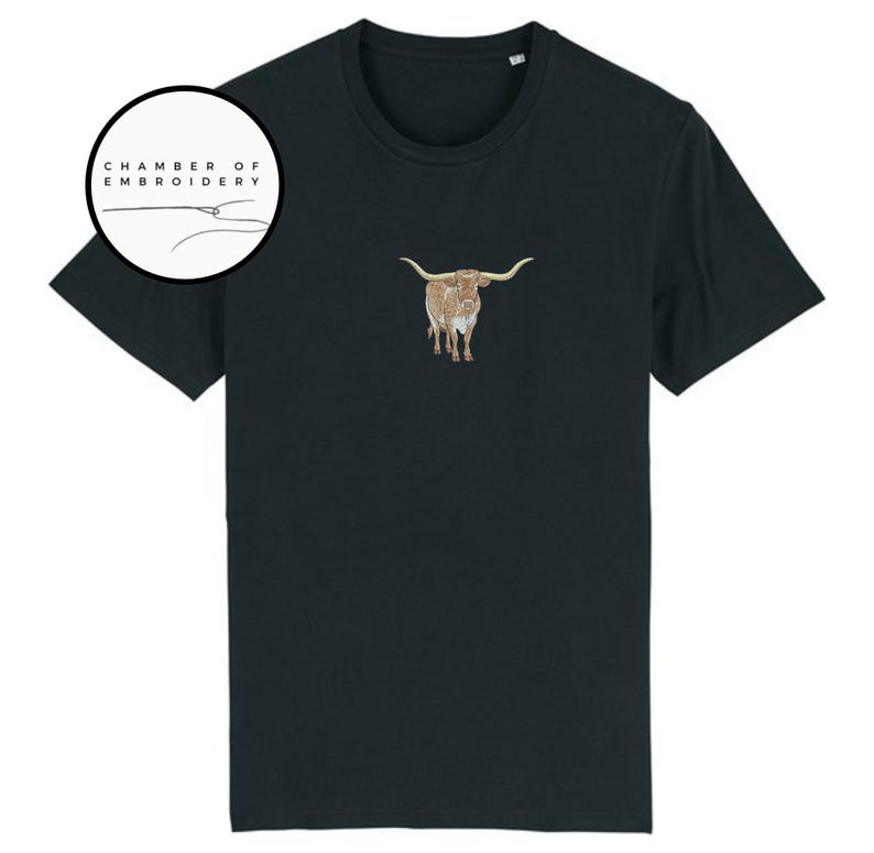 May include: A black t-shirt with a brown and white embroidered longhorn steer on the front. The shirt has a crew neck and short sleeves. The text "Chamber of Embroidery" is in a circle above the steer.