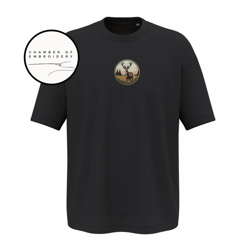 May include: A black short-sleeved t-shirt featuring a circular embroidered patch on the chest depicting a deer in a field with trees at sunset. A circular logo in the upper left corner contains the text CHAMBER OF EMBROIDERY with a needle icon.