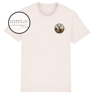 May include: A light pink short-sleeve t-shirt featuring a circular embroidered patch on the left chest depicting a stag in a field. A circular logo in the upper left corner contains the text CHAMBER OF EMBROIDERY with a needle and thread graphic.