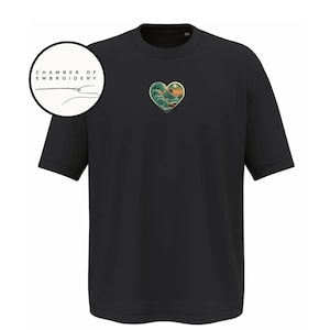 Może przedstawiać: Czarny t-shirt z kr&oacute;tkim rękawem z małym haftem w kształcie serca na piersi, przedstawiającym stylizowaną falę oceaniczną i zach&oacute;d słońca. Okrągłe logo w lewym g&oacute;rnym rogu zawiera napis CHAMBER OF EMBROIDERY oraz ikonę igły z nitką.