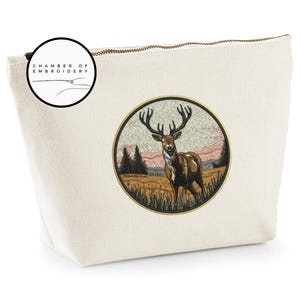 May include: A cream-colored canvas pouch featuring a circular embroidered patch of a stag in a field with trees and a sunset sky. The patch is bordered in gold. A circular logo in the top left corner reads CHAMBER OF EMBROIDERY.