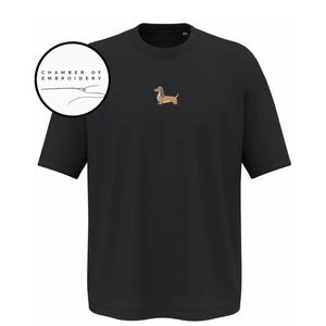 May include: Black short-sleeved t-shirt with a small embroidered dachshund dog on the chest. The dog is brown and tan with a long body and short legs. The text "CHAMBER OF EMBROIDERY" is in a circle in the upper left corner.