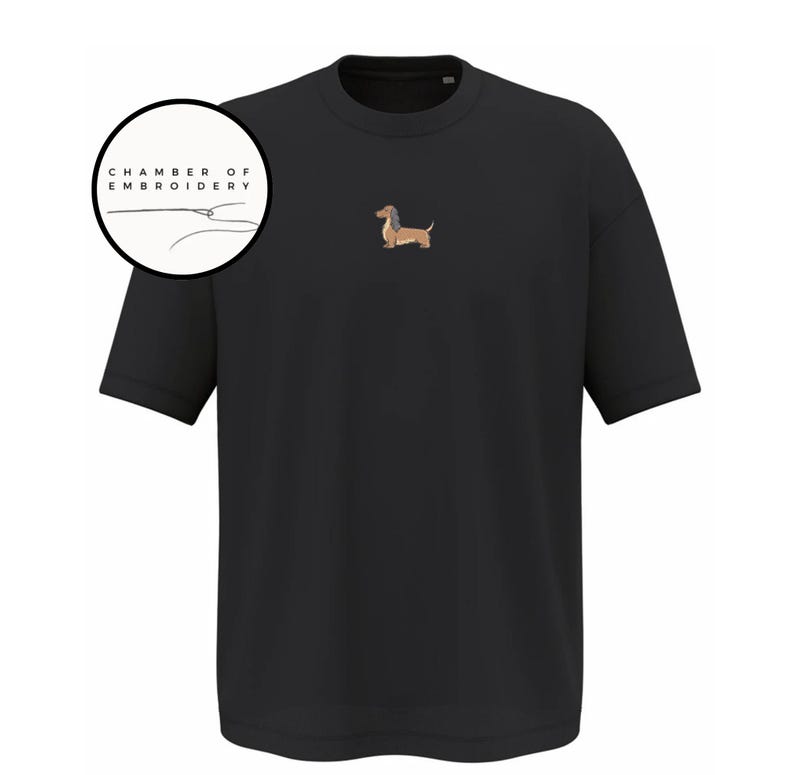 May include: Black short-sleeved t-shirt with a small embroidered dachshund dog on the chest. The dog is brown and tan with a long body and short legs. The text "CHAMBER OF EMBROIDERY" is in a circle in the upper left corner.