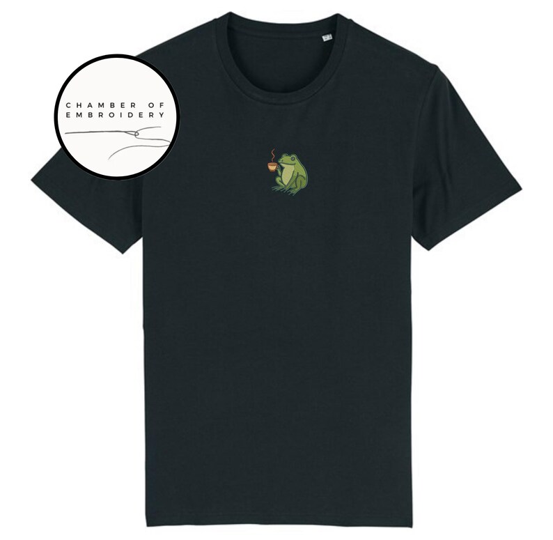 May include: Black t-shirt featuring a small embroidered design of a green frog holding a cup of coffee. The shirt has short sleeves and a crew neck. The logo "CHAMBER OF EMBROIDERY" is in a circle on the left side of the shirt.