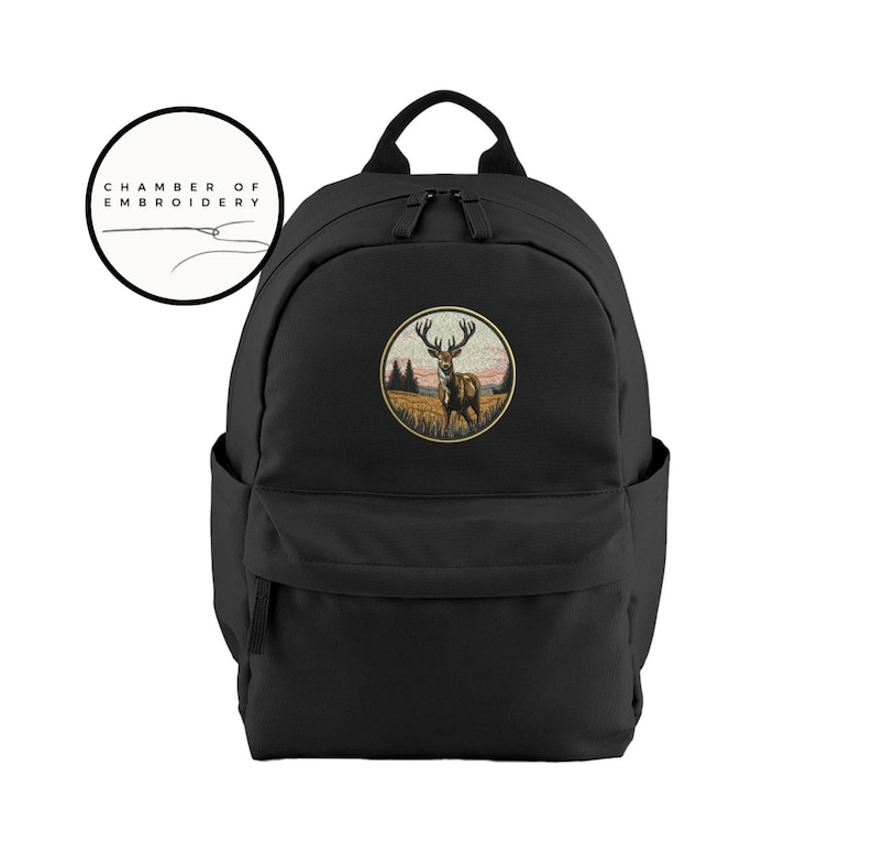 May include: A black backpack featuring a circular embroidered patch on the front. The patch depicts a deer standing in a field with trees and a sunset sky. Above the backpack is a circular logo with the text Chamber of Embroidery.