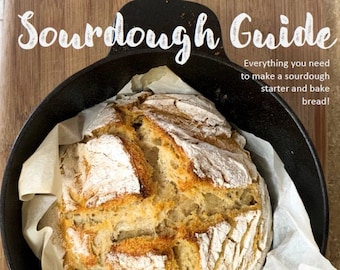 May include: A loaf of freshly baked sourdough bread in a black cast iron pan, lined with parchment paper. The bread has a golden-brown crust with a scored top. The image includes the text "Sourdough Guide" and "Everything you need to make a sourdough starter and bake bread!"