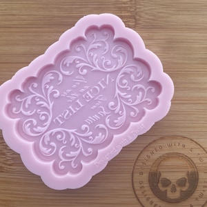 Könnte beinhalten: Eine hellrosa Silikonform mit einem verzierten, gerollten Rand. Die Form zeigt die Worte "Nice List" in einer dekorativen Schriftart. Der Satz "Designed with a Twist" ist ebenfalls sichtbar.