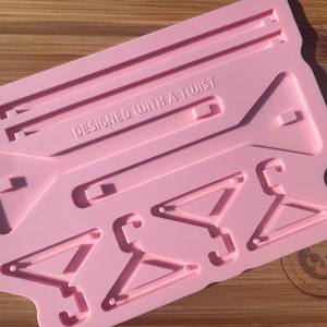 Può includere: Stampo in silicone rosa con il testo "DESIGNED WITH A TWIST" e quattro forme geometriche, tra cui tre triangoli e un rettangolo.