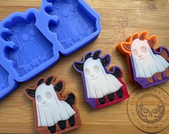 May include: A silicone mold for making ghost-shaped candy or soap. The mold is blue and features four ghost designs with different colored accents. The ghosts have horns and are wearing a sheet. The mold is designed with a skull logo and the text "Designed with a Twist".