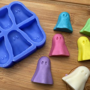 May include: A silicone mold shaped like six ghosts, with six finished ghost-shaped candies in various colors: light blue, pink, yellow, green, white, and purple. The mold is blue and has a textured surface.