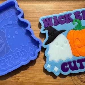 May include: A blue silicone mold with a design of a ghost wearing a witch hat, a pumpkin, and the text "Wicked Cute".