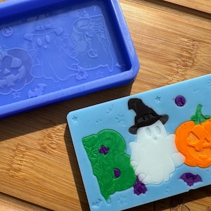 May include: A blue silicone mold for making Halloween-themed soap or resin crafts. The mold features a ghost, a pumpkin, and the letters "BOO" in a green, purple, and orange color scheme.