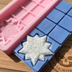 May include: Two silicone molds for making wax melts. One mold is pink and has a snowflake design. The other mold is blue and has a star design. Both molds are on a wooden surface.