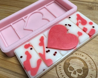 Op de afbeelding: Een roze wax melt mal met een hartvormig ontwerp, naast een wax melt bar met een groot hart en rode accenten. De wax melts zijn wit met rode spetters en glitter. De mal is rechthoekig met hartvormige uitsparingen.
