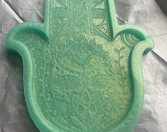 May include: A light green hamsa hand tray with intricate patterns. The tray is made of resin and has a smooth, glossy finish.