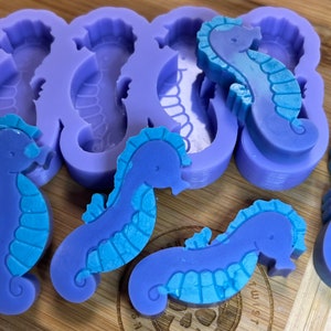 May include: Purple and blue silicone molds for making seahorse-shaped soap or resin crafts. The molds are shown with finished seahorse soaps.