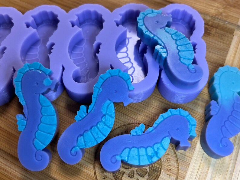 May include: Purple and blue silicone molds for making seahorse-shaped soap or resin crafts. The molds are shown with finished seahorse soaps.