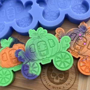 May include: Three pumpkin carriage shaped silicone molds. The molds are green, orange, and purple. The molds are designed with a pumpkin on top of a carriage. The molds are designed with a twist.