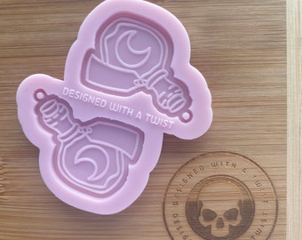 Könnte beinhalten: Eine rosa Silikonform mit zwei Designs von Flaschen in Form eines Halbmondes. Die Form ist mit "Designed with a Twist" beschriftet.