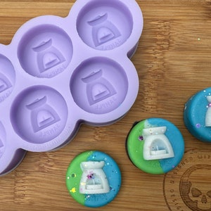 May include: A purple silicone mold with six round cavities, each featuring a raised design of a small oil burner. Three finished oil burner wax melts are shown, two with green and blue swirls and one with white and blue swirls.