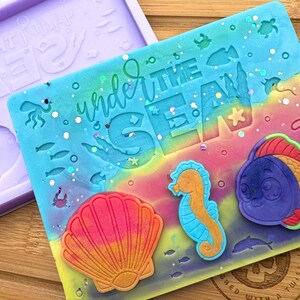May include: A silicone mould for resin crafts featuring a rainbow ombre background with the text "Under the Sea". The mould includes a seashell, a seahorse, and a fish.