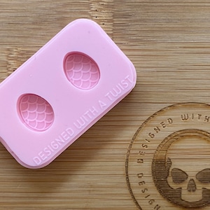 May include: Pink silicone mould with two egg-shaped cavities, each with a scale pattern. The mould is labelled "DESIGNED WITH A TWIST".