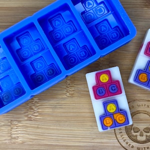 May include: A blue silicone mould with six sections, each containing a three-piece puzzle with the letters A, B, and C. There are two sets of the puzzle made of purple, orange, and yellow plastic.