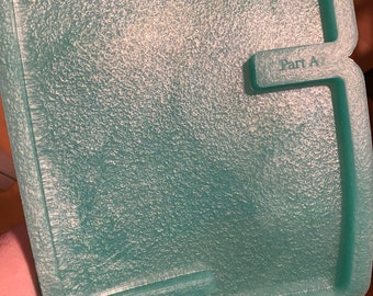 May include: A teal-coloured, textured plastic tray with the text "Designed with a Twist" and "Part A". The tray has a unique shape with curved edges and a textured surface. It appears to be a component of a larger item.