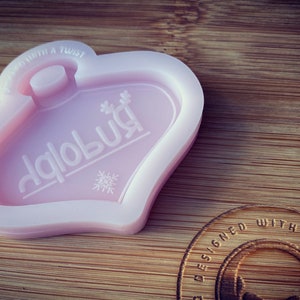May include: Pink silicone mold shaped like a heart with a snowflake and the word "dablobu" inside. The mold is designed for making resin crafts.