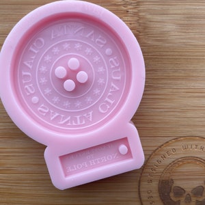 Op de afbeelding: Roze siliconen mal in de vorm van een knoop met de tekst "ATLANTA" en "GUAD" rond de knoop. De mal heeft een kleine cirkel aan de onderkant met de tekst "NORTH GORE" en "IT'S GREAT TO BE HOME".