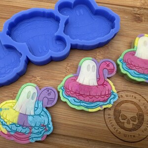 May include: A silicone mold with three ghost shapes, and three finished resin pieces of ghosts in colorful inflatable rings. The resin pieces are on a wooden surface with a logo that says "Designed with a twist".