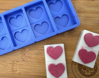 Op de afbeelding: Een blauwe siliconen mal met zes hartvormige holtes. Naast de mal zijn twee witte staven met drie roze hartvormige was smelt te zien.