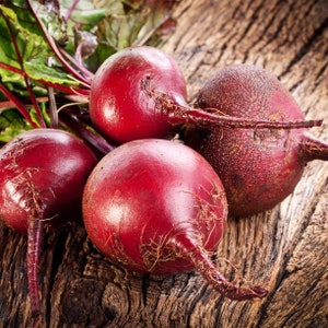 May include: Four red beets with green leafy tops on a rustic wooden surface.