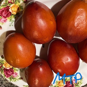 May include: A collection of ripe, reddish-orange fruits, possibly persimmons, arranged on a decorative plate with floral patterns. The fruits vary slightly in size and shape, with smooth, glossy skin. The plate has a gold trim.