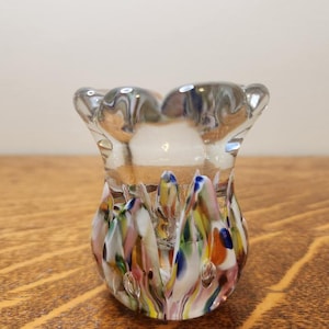 May include: A small, clear glass vase with a scalloped rim and a colorful, marbled base. The base features swirls of pink, blue, green, yellow, and white.