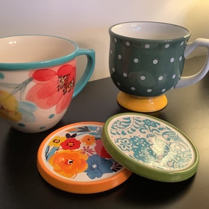 Pu&ograve; includere: Due tazze in ceramica con motivi floreali e a pois, e due sottobicchieri abbinati con motivi floreali e paisley. Le tazze e i sottobicchieri sono in tonalit&agrave; di blu, verde, giallo, arancione e rosso.