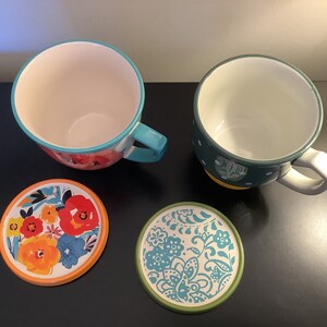 Pu&ograve; includere: Due tazze in ceramica con motivi floreali colorati e sottobicchieri abbinati. Una tazza &egrave; turchese e bianca con pois gialli, l'altra &egrave; arancione, rossa e blu con un motivo floreale. I sottobicchieri sono rotondi e presentano gli stessi motivi delle tazze.