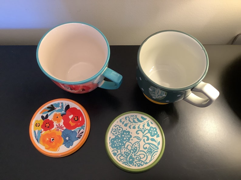 Pu&ograve; includere: Due tazze in ceramica con motivi floreali colorati e sottobicchieri abbinati. Una tazza &egrave; turchese e bianca con pois gialli, l'altra &egrave; arancione, rossa e blu con un motivo floreale. I sottobicchieri sono rotondi e presentano gli stessi motivi delle tazze.