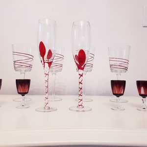 May include: Set of nine clear glass wine glasses with red and white swirl designs. The glasses include four tall champagne flutes, two shorter wine glasses, and three small shot glasses.