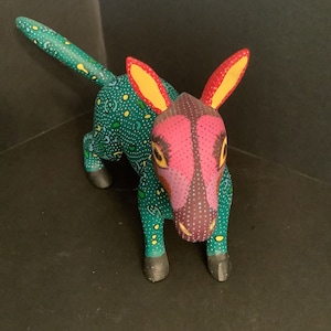 May include: A hand-painted wooden donkey figurine with a green, pink, yellow, and black color scheme. The donkey has a spotted pattern and large ears.