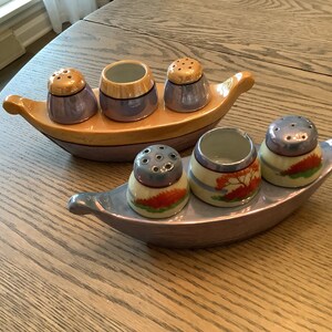 May include: A set of six vintage salt and pepper shakers in the shape of boats. The shakers are made of ceramic and have a blue and gold glaze. The boats are decorated with floral designs.