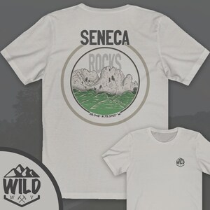 May include: White t-shirt with a circular graphic on the back. The graphic features a mountain range with the text "Seneca Rocks" and coordinates "38.348&deg; N 79.3762&deg; W". The front of the shirt has a small logo with the text "WILD" and a mountain range graphic.