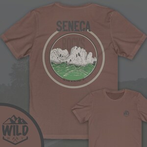 May include: A brown t-shirt with a graphic of a mountain range and the text "Seneca Rocks" in a circle. The t-shirt also has a small logo with the text "WILD" on the front.